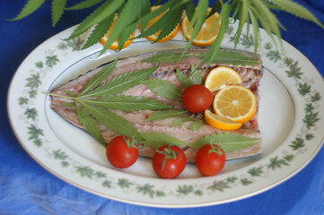 cannabis food. classic cannabis leafs lies on fresh fish. homemade fish food with young leaves of marijuana