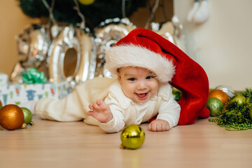 Obraz na płótnie Canvas Cute smiling baby is lying under a festive Christmas tree and playing with gifts. Christmas and New Year celebrations