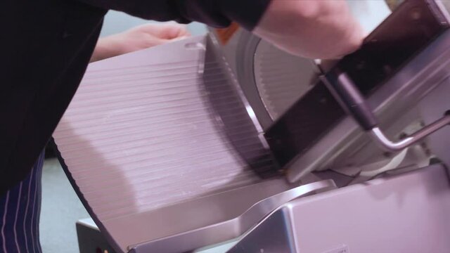 A uniformed deli worker uses an industrial slicer to prepare deli meats and cheese