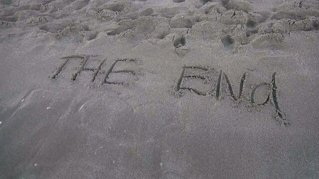 the inscription "the end" with a heart painted on the sand is washed away by waves into the sea