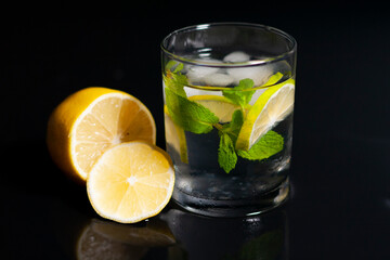 In the center of the screen are a glass of water, ice cubes, a sprig of mint and a slice of lemon. Next to a sliced lemon. 
