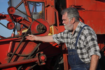 Adult farmer or mechanic touching and examining belt at combine harvester