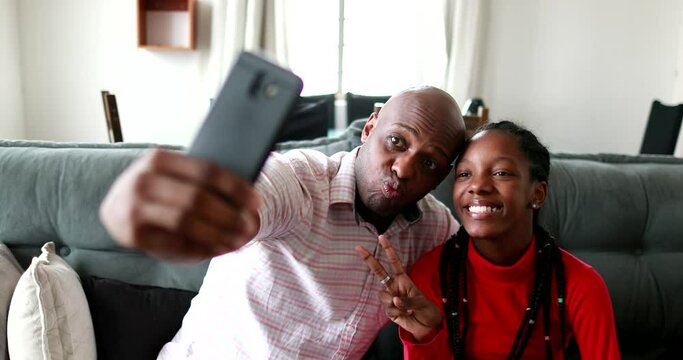 Black father and daughter taking selfie together at home couch