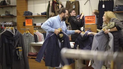 Wide shot of Caucasian men and women fighting for clothes in shop during black friday sales. Male and female clients rushing to buy goods with best price. Fashion and lifestyle.