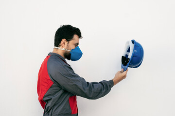 Attractive worker profile man with face mask for protection puts on the helmet before working on...
