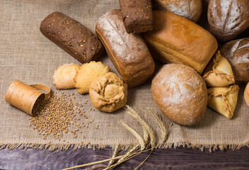 Assortment of bread, ears and grains of wheat on wooden table
