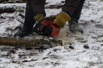 A man cuts wood with a power saw in the snow.