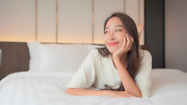 A pretty young woman lying on her stomach on a big comfortable bed leans her chin on her hand and smiles.