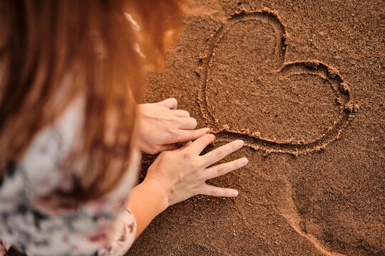 Drawing of heart on sand. The girl draws with fingers in sand.