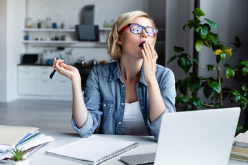 young blonde woman in eyeglasses working from home and yawning