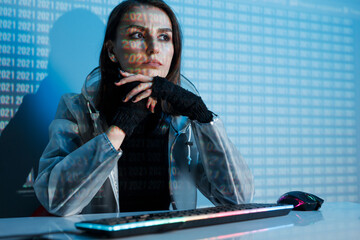 Internet, crime, cyber attack, system breaking concept. Blue neon light background. Woman hacker is working on a code with digital interface all around.