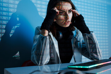 Internet, crime, cyber attack, system breaking concept. Blue neon light background. Woman hacker is working on a code with digital interface all around.