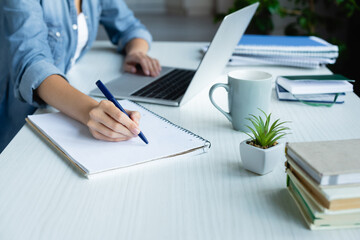 cropped view of woman making notes in notebook and typing on laptop