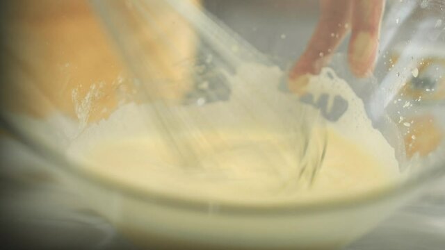 Chef whisks vegan egg yolk in a glass bowl with a wire whip eggbeater. Close up. Shot in 4K.