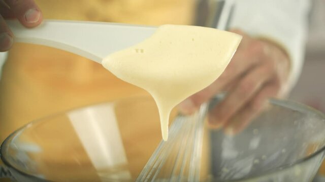 Chef puts some egg yolk cream with a plastic spoon out of a glass bowl and holds it up. SOme drips back into the bowl. Close up with shallow depth. Shot in 4K.