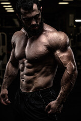 Fototapeta na wymiar strong sport athlete male with beard and perfect physique body in dark fitness gym