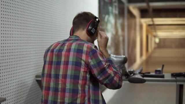 Rare view of a man in indoors shooting range putting on protective headphones