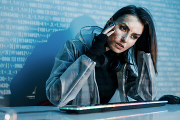 Internet, crime, cyber attack, system breaking concept. Blue neon light background. Woman hacker is working on a code with digital interface all around.
