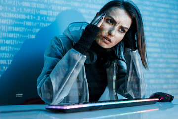 Internet, crime, cyber attack, system breaking concept. Blue neon light background. Woman hacker is working on a code with digital interface all around.