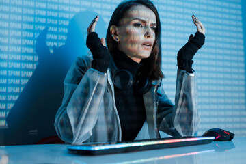 Internet, crime, cyber attack, system breaking concept. Blue neon light background. Woman hacker is working on a code with digital interface all around.