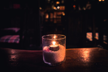 Isolated tealight inside a glass illuminating a dark scene and reflections on a wooden table and a nice bokeh background