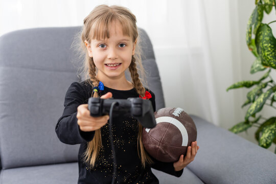 Little girl holding a rugby ball and joystick for playing video games