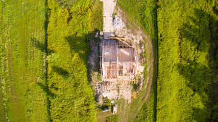 Top-down view on detached house under construction. House in basic state. Located on green plot in small village. Wooden roof structure. Meadows around.