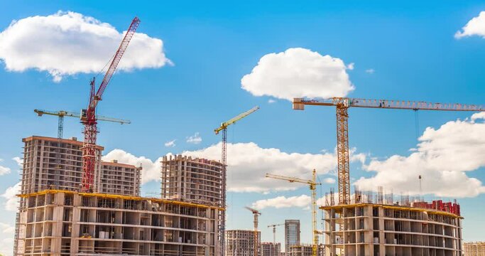 Large construction site with busy cranes. Tower cranes working on a construction site lifts a load at high-rise building. Summer blue sky. Time-lapse