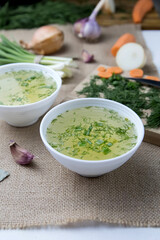 Two cups with vegetable broth are on the table, vegetables lie next to it, light, vertical photo