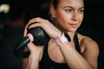 Close-up face of a beautiful young athlete woman holding black kettlebell with both hands during...