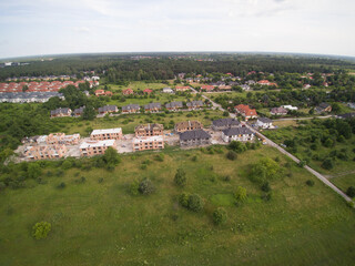 Aerial panorama on settlements of detached house under construction. House In basic state. Located on green plot in small village. Wooden roof structure. Meadows around.