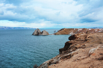 A steep coast, rocks stick out from the turquoise water. Lake Baikal, Olkhon Island, Shamanka mountain