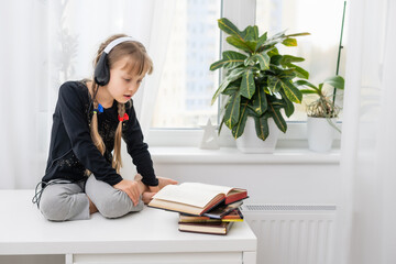 Adorable little girl with headphones sitting on the table at home