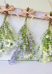 Various bright bouquet of dried flowers hanging on rope against wooden background, making dried flowers modern decoration for home interior