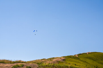 Fototapeta na wymiar Paraglider flying over Carpathian mountains against clear sky in summer day