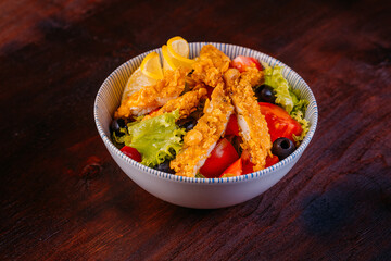 Healthy salad with fillet chicken, tomatoes, lettuce, olives, lemon and sauce in bowl on wooden background. Healthy food, clean eating, dieting, top view
