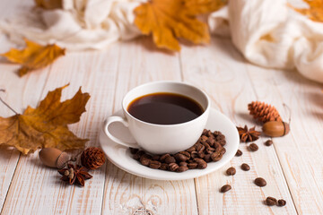 White scarf, a cup of coffee with scattered coffee beans, dry yellow leaves on a wooden table. Autumn mood, copy space.