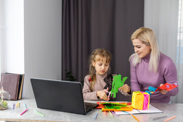 Child with mother have a fun cutting out scissors paper in preschool. mother and daughter make paper crafts