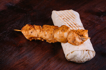 Delicious turkish doner kebab with chicken, onion, tomatoes, lettuce, parsley, carrot, cucumbers and sauce isolated on dark wooden background 