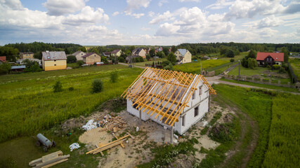 Aerial view on detached house under construction. House In basic state. Located on green plot in small village. Wooden roof structure. Meadows around.
