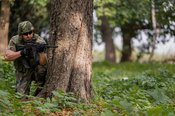 Naklejka premium Soldier aiming the target. Military action in a forest. Ground gun battle. Fully equipped military forces in operations. Boots on the ground. Airsoft recreation sports. Soldier in tactical equipment.