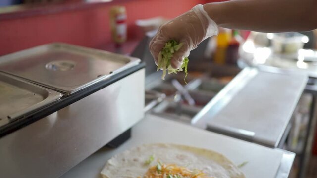 Lettuce being dropped on a soft taco shell in slow motion.