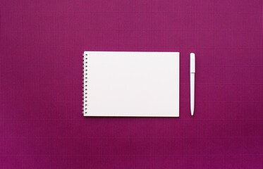 Notebook with white sheets on a spring with empty pages, white pen, light lilac background. View from above, place for text.