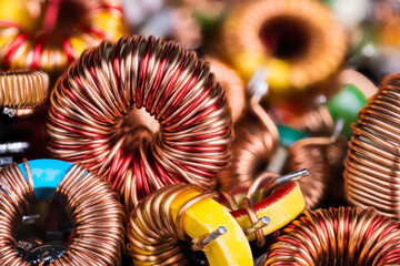 Fototapeta na wymiar Toroidal electronic inductors on heap in electrotechnical background. Closeup of beautiful induction coils with copper wire winding on magnetic ferrite core. Colored electrical engineering components.