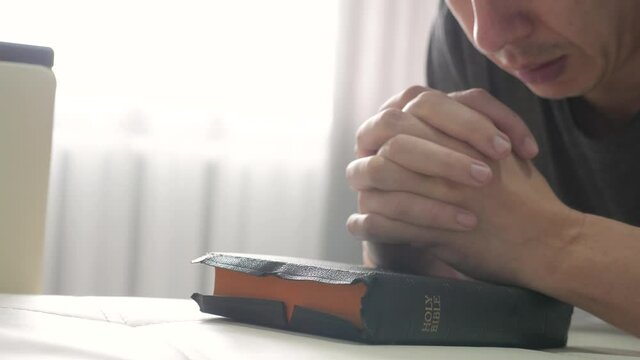 man praying indoors lifestyle at bedtime on bible. religion concept evening prayer human brunette hands on bible praying by bed