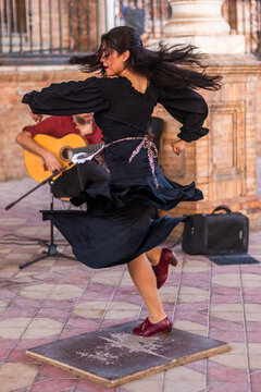 Stock photo of a flamenco dancer dancing and feeling flamenco with and unrecognizable guitarist behind. Woman outdoors dancing flamenco with a black dress and red lips.