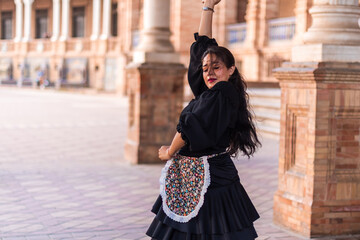 Stock photo of a flamenco dancer dancing and feeling flamenco. Woman outdoors dancing flamenco with a black dress and red lips. - obrazy, fototapety, plakaty