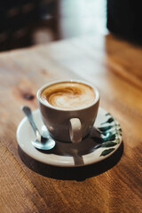Front view of a coffee in a white cup on a plate with green leaves drawn on a wooden table. Breakfast concept.