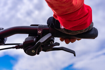 The hand of a woman with a fingerless glove, holding the handlebars of a bicycle, with a blue sky and clouds in the background