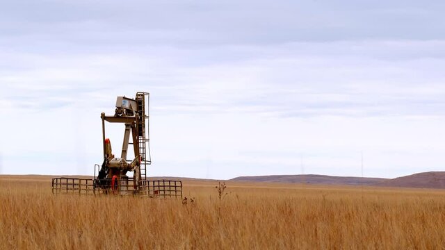 Oil Well Pump Jack pumping crude oil for fossil fuel energy. American Petroleum Oil and Gas Industry equipment extracting from a field on a prairie in America. Zoom out reveals second well.